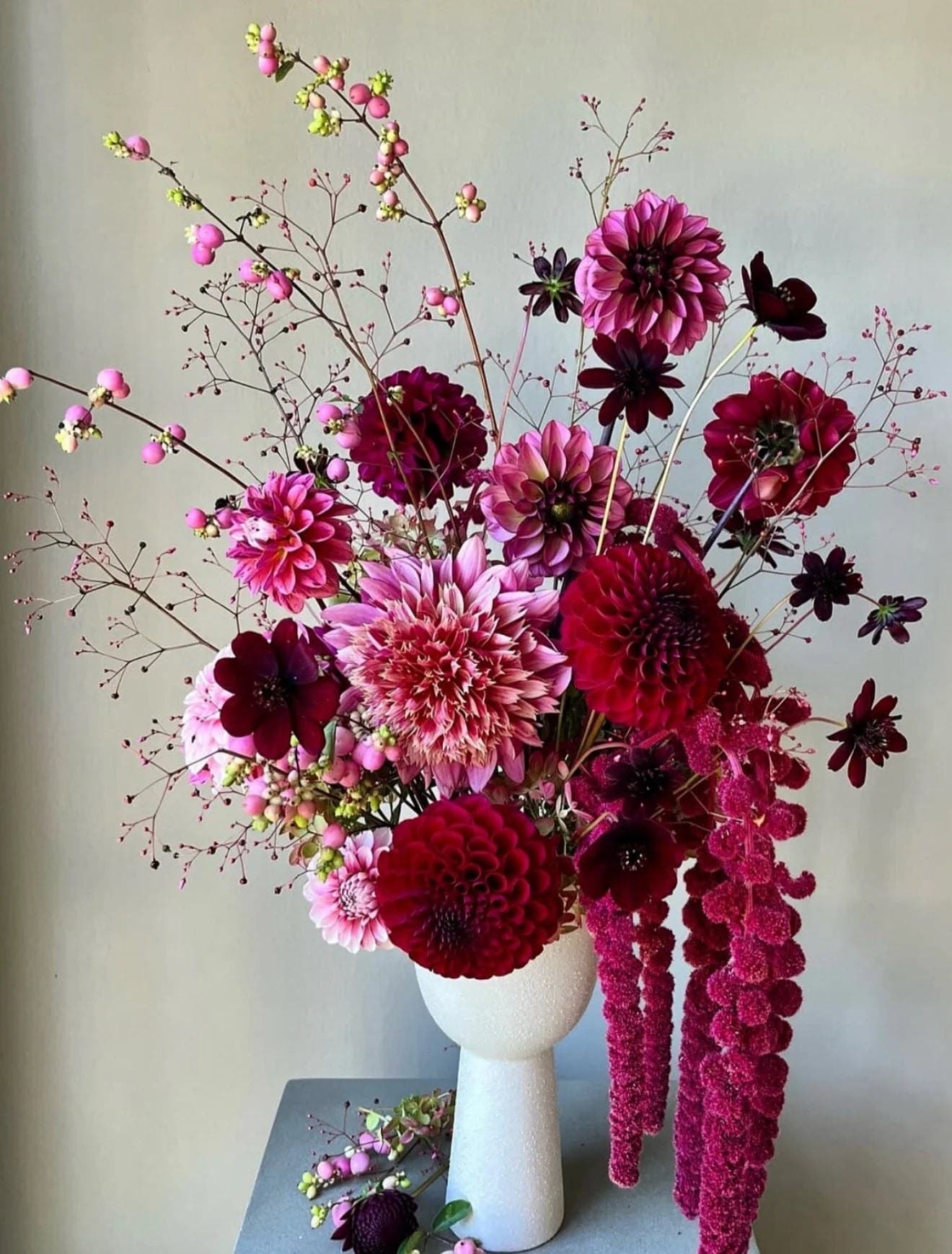 Fuchsia and burgundy dahlias with chocolate cosmos, snowberry and trailing amaranthus in a white vase