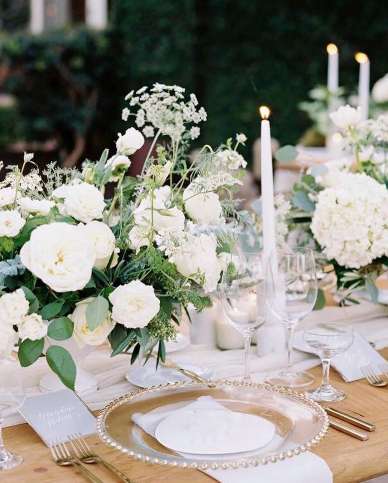 A wedding table close up: white roses and hydrangea, tapered candles, linen