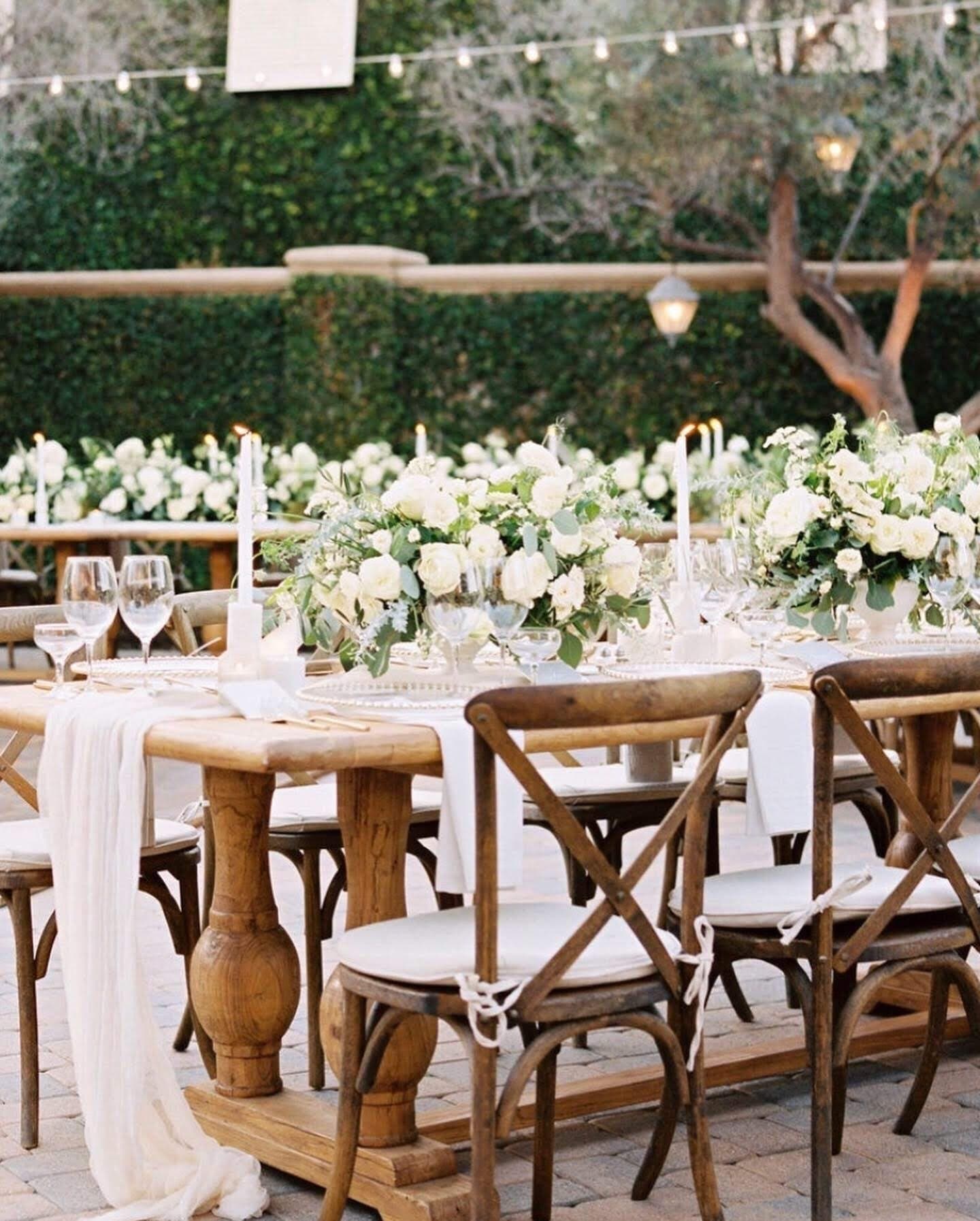 Long wedding tables laid outdoors, with white and green florals down the centre
