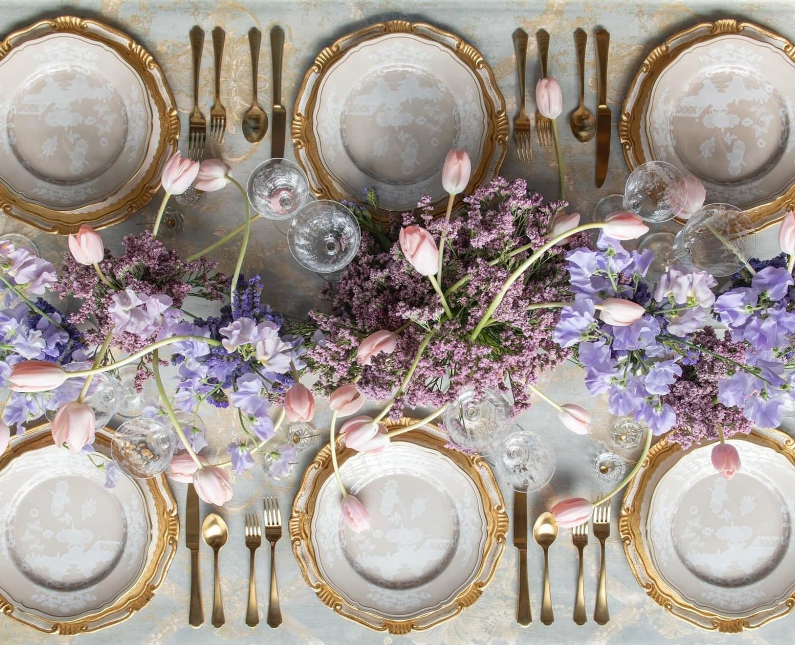 A long table dressed with lilac florals and gold place settings